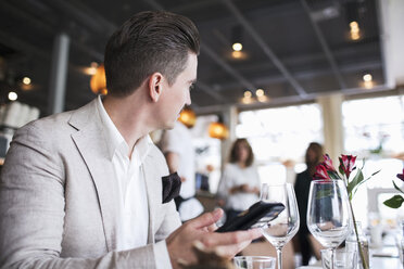 Businessman looking away while holding mobile phone at restaurant - MASF02658