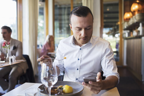 Geschäftsmann isst zu Mittag und benutzt dabei ein Mobiltelefon im Restaurant - MASF02665