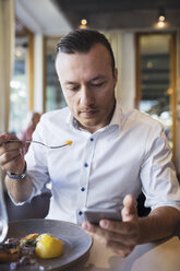 Geschäftsmann, der ein Mobiltelefon benutzt, während er in einem Restaurant zu Mittag isst - MASF02666