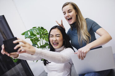 Cheerful female bloggers taking selfie through smart phone in creative office - MASF02672
