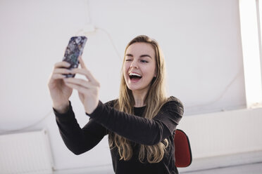 Fröhliche Bloggerin zwinkert, während sie ein Selfie mit ihrem Smartphone im Büro macht - MASF02673