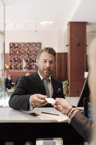 Geschäftsmann gibt der Rezeptionistin an der Hotelrezeption eine Kreditkarte, lizenzfreies Stockfoto