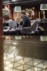 Businesswoman signing agreement by male partner sitting in hotel reception - MASF02693