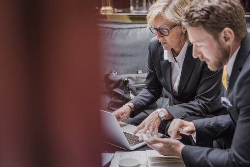 Geschäftsleute benutzen Laptop und Mobiltelefon während einer Besprechung an der Hotelrezeption - MASF02696