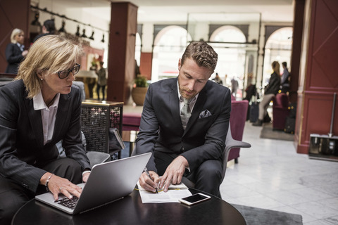 Geschäftsfrau sieht ihren Partner bei der Vertragsunterzeichnung an der Hotelrezeption, lizenzfreies Stockfoto