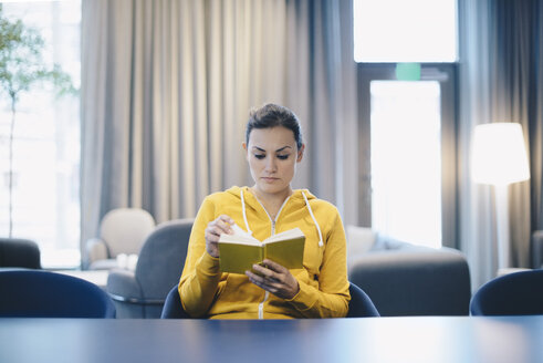 Businesswoman reading book in office lobby - MASF02704
