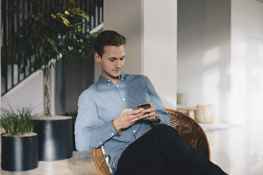 Geschäftsmann, der ein Smartphone benutzt, während er auf einem Stuhl im Büro sitzt - MASF02705