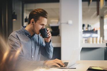 Businessman drinking coffee while using laptop at desk in office - MASF02713