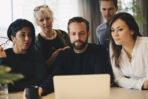 Business colleagues using laptop at conference table together in board room - MASF02715