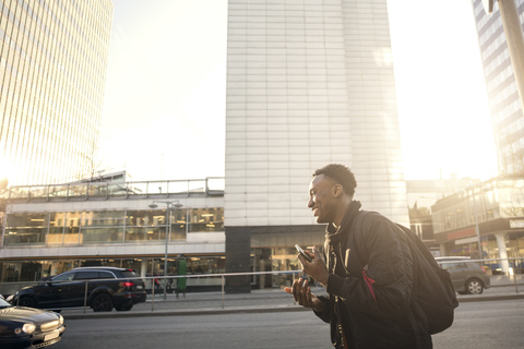 Smiling teenager gesturing while holding phone against buildings in city stock photo