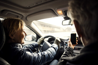 Lächelnde ältere Frau, die Auto fährt und neben einem Mann sitzt, der ein Selfie mit seinem Smartphone macht - MASF02740