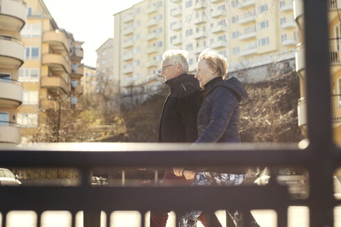 Lächelndes älteres Paar, das am Straßenrand gegen Gebäude in der Stadt läuft - MASF02742