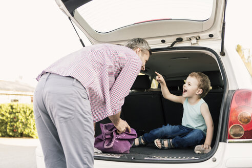 Der Sohn zeigt auf den Vater, während er im offenen Kofferraum sitzt - MASF02746