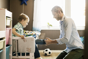 Lächelnder Vater, der seinen Sohn zu Hause an einem sonnigen Tag anzieht - MASF02748