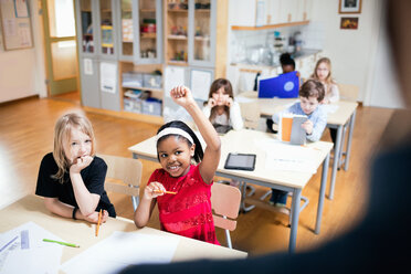 Smiling student with hand raised sitting in classroom - MASF02755