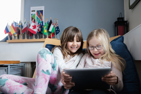 Lächelnde Freunde benutzen ein digitales Tablet, während sie sich auf dem Sofa in der Schule ausruhen, lizenzfreies Stockfoto