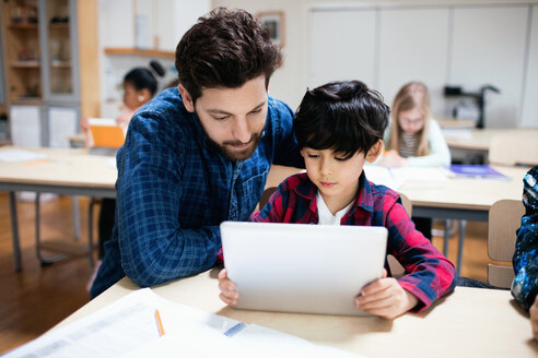 Lehrer, der einem männlichen Schüler bei der Verwendung eines digitalen Tablets hilft, während er im Klassenzimmer sitzt - MASF02759