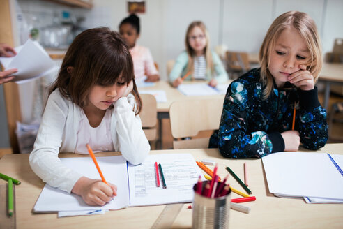 Schüler schreiben auf Papier am Schreibtisch im Klassenzimmer - MASF02762