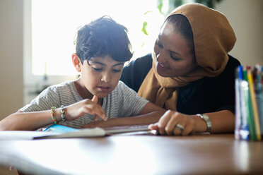 Lächelnde Mutter, die ihrem Sohn beim Lernen zu Hause mit einem digitalen Tablet hilft - MASF02765