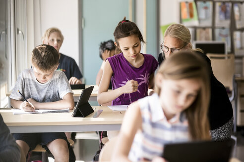 Lehrer, der einer Schülerin durch einen Jungen im Klassenzimmer hilft - MASF02770