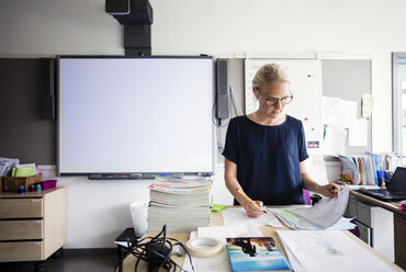 Lehrer schreibt auf Papier gegen leere Tafel im Klassenzimmer - MASF02773