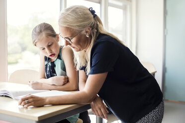 Lehrerin hilft Schülerin mit Buch im Klassenzimmer - MASF02774