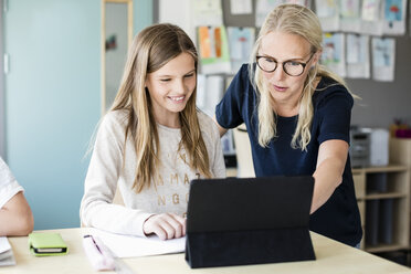 Teacher assisting happy girl in using digital tablet at school - MASF02777