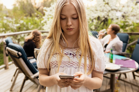 Teenage girl using smart phone at yard with family sitting in background stock photo