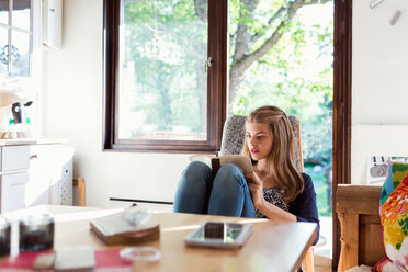 Teenager-Mädchen liest ein Buch, während sie auf einem Stuhl zu Hause sitzt - MASF02786