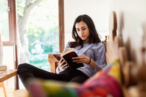 Teenager-Mädchen, das auf dem Sofa sitzend ein Buch liest - MASF02787