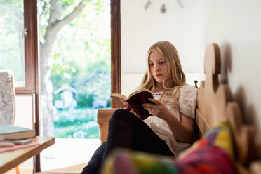 Teenager-Mädchen liest ein Buch, während sie zu Hause auf dem Sofa sitzt - MASF02788