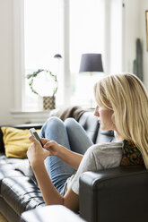 Teenage girl using phone while reclining on sofa at home - MASF02797