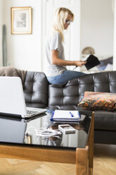 Technik und Buch am Tisch mit Teenager, der auf dem Sofa im Wohnzimmer sitzt und ein Dokument liest - MASF02799