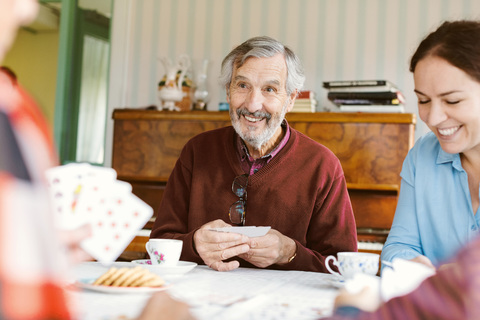 Smiling senior man playing cards with family at home stock photo