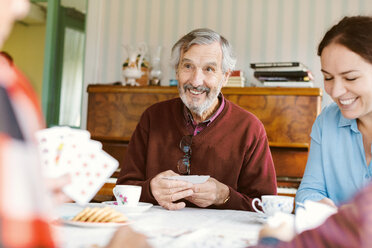 Lächelnder älterer Mann, der mit seiner Familie zu Hause Karten spielt - MASF02803