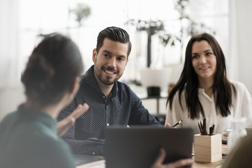 Smiling colleagues looking at businesswoman showing laptop during meeting - MASF02811