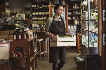 Smiling owner carrying vegetable crate while walking in store - MASF02815