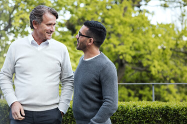 Smiling multi-ethnic friends talking while standing against hedge in yard - MASF02818