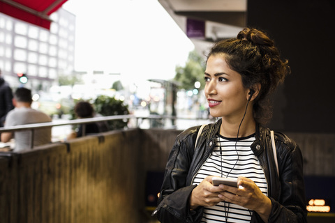 Lächelnde Frau hört Musik über das Telefon in der U-Bahn-Station, lizenzfreies Stockfoto