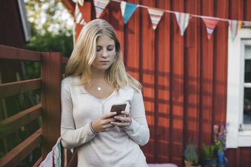 Teenager-Mädchen lehnt sich an den Zaun und schreibt SMS gegen das Haus im Hinterhof - MASF02825