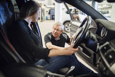 Älterer Experte im Gespräch mit einer Kundin im Auto sitzend in einer Werkstatt - MASF02831