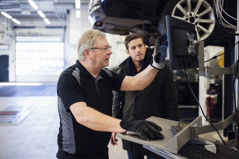 Senior mechanic showing computer monitor while discussing with customer at repair shop - MASF02833