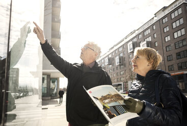 Ältere Frau liest einen Katalog, während ein Mann auf ein Glasfenster in der Stadt zeigt - MASF02841