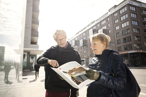 Älteres Paar liest Katalog an einem Gebäude in der Stadt, lizenzfreies Stockfoto