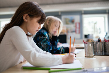 Seitenansicht von Schülern, die am Schreibtisch im Klassenzimmer auf Papier schreiben - MASF02854