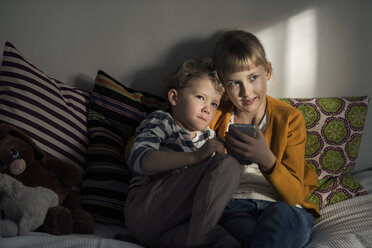 Siblings using mobile phone while sitting on sofa at home - MASF02858