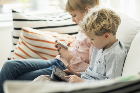 Geschwister nutzen Technologien auf dem Sofa zu Hause, lizenzfreies Stockfoto