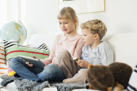 Geschwister nutzen ein digitales Tablet, während sie zu Hause auf dem Sofa sitzen, lizenzfreies Stockfoto