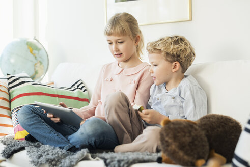 Geschwister nutzen ein digitales Tablet, während sie zu Hause auf dem Sofa sitzen - MASF02864