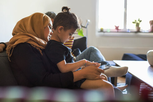 Seitenansicht von Mutter und Sohn bei der Nutzung eines digitalen Tablets, während sie zu Hause auf dem Sofa sitzen - MASF02867